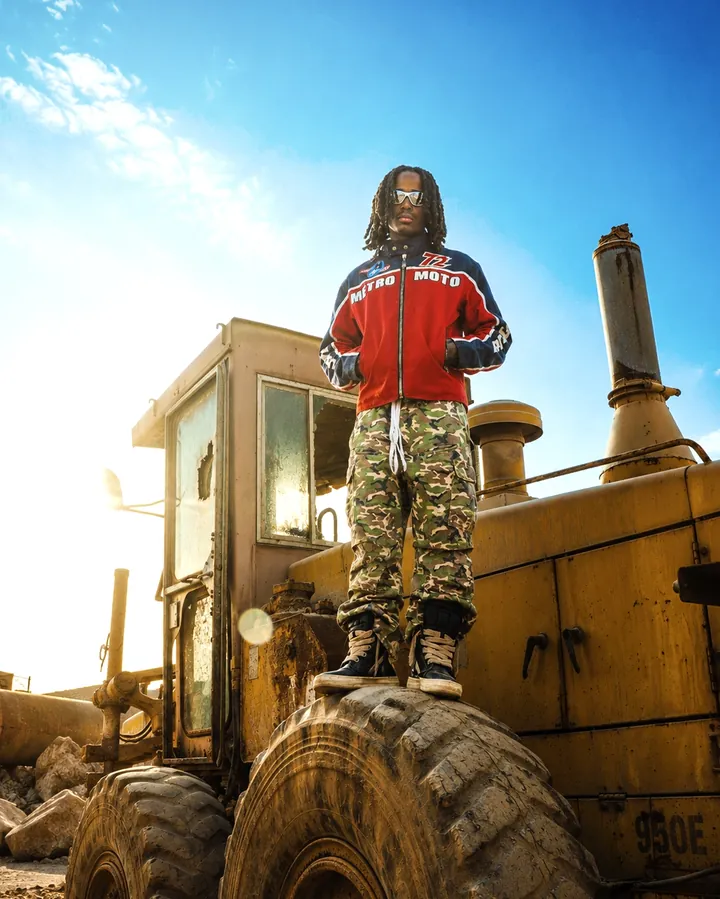 Low-angle stance on an excavator tyre in a red jacket and camouflage trousers.