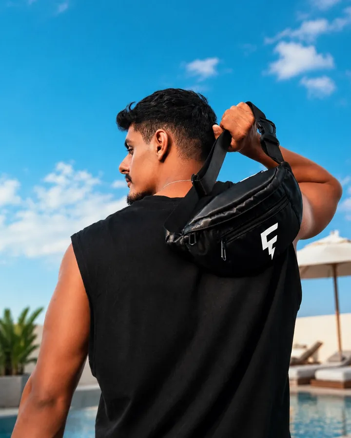 Rear view of a black belt bag carried over the shoulder against a blue sky.