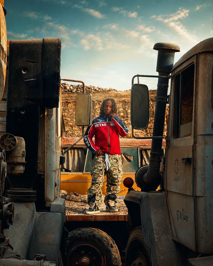 Standing on a truck bed among scrap metal in a red and blue jacket.