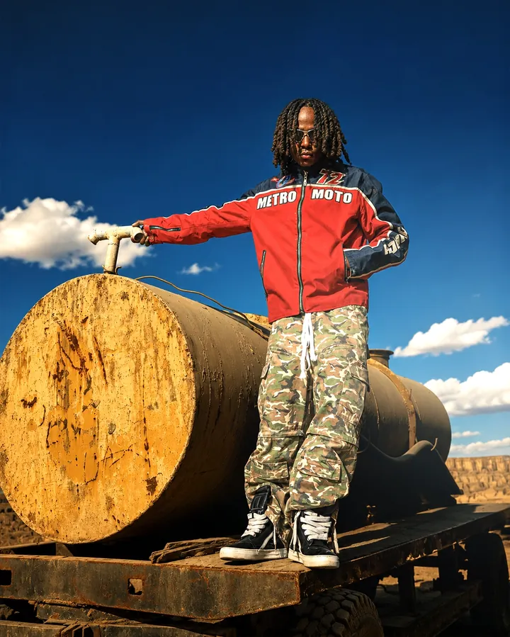 Standing on a rusted tank, one hand on the metal lever, under a clear blue sky.