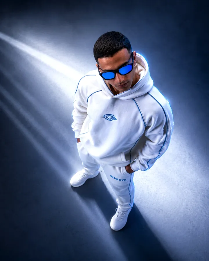 Overhead frame of a white tracksuit and white sneakers on a floor cut by a beam of light.